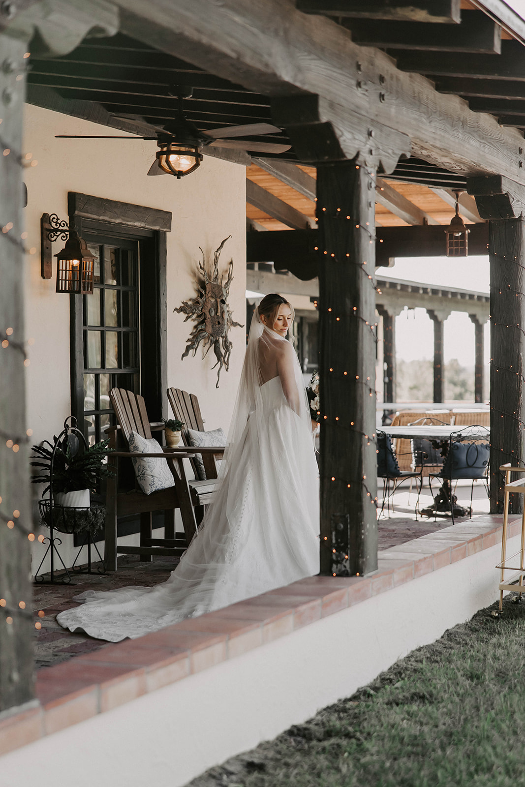 bridal portrait porch la hacienda snow hill brooksville - A Fall Wedding at La Hacienda on Snow Hill in Brooksville, FL Bride in a flowing white gown and cathedral veil standing on the rustic covered porch at La Hacienda on Snow Hill wedding venue in Brooksville Florida