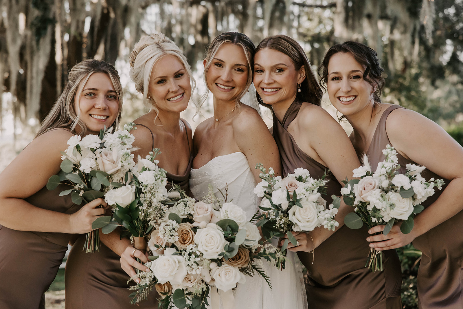 bride bridesmaids bouquets la hacienda brooksville florida - A Fall Wedding at La Hacienda on Snow Hill in Brooksville, FL Bride in white strapless gown surrounded by four bridesmaids in taupe dresses holding white and blush rose bouquets at La Hacienda on Snow Hill wedding venue in Brooksville Florida near Tampa