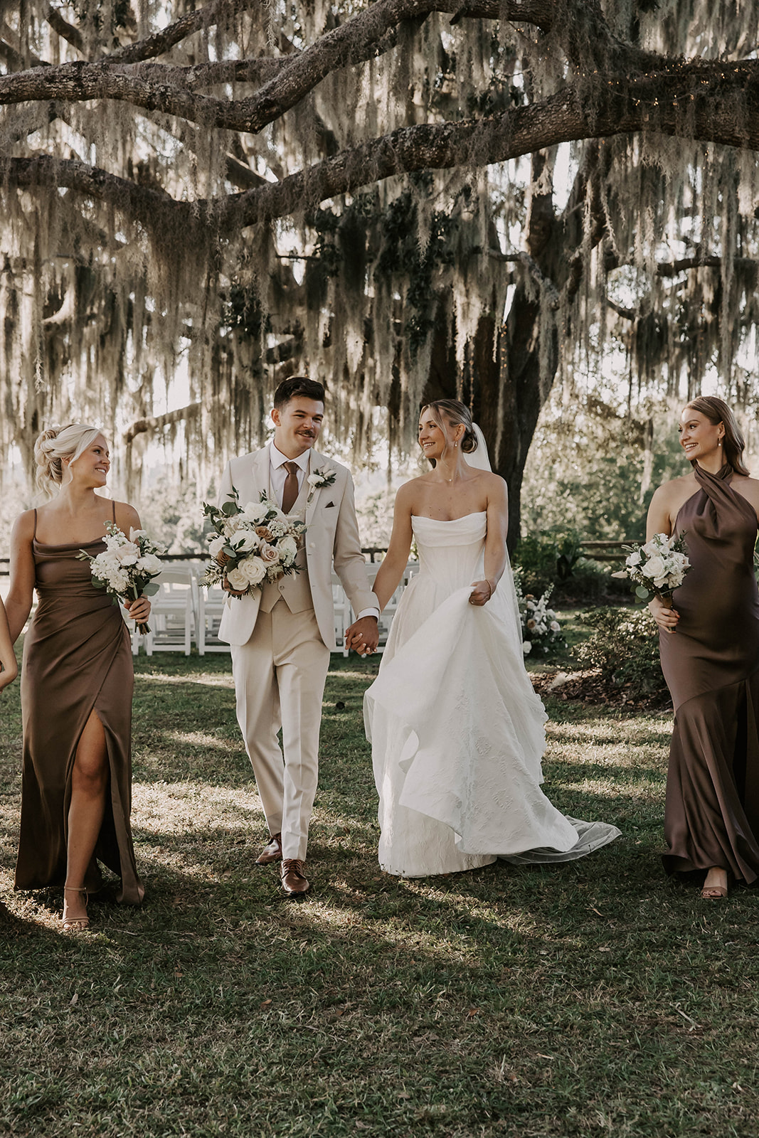 bride groom bridesmaids spanish moss oak tree brooksville florida - A Fall Wedding at La Hacienda on Snow Hill in Brooksville, FL Bride and groom walk hand in hand with bridesmaids in brown satin gowns beneath a dramatic Spanish moss oak tree at La Hacienda on Snow Hill wedding venue in Brooksville Florida near Tampa
