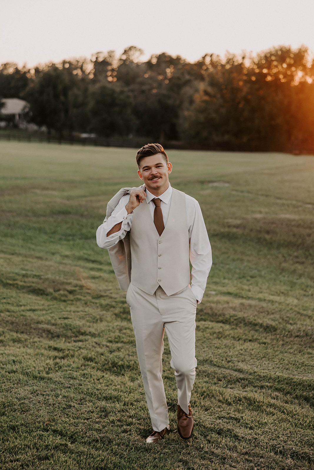 groom portraits golden hour la hacienda snow hill - A Fall Wedding at La Hacienda on Snow Hill in Brooksville, FL Groom in a cream three-piece suit with brown tie carrying his jacket over his shoulder during golden hour portraits at La Hacienda on Snow Hill wedding venue in Brooksville Florida