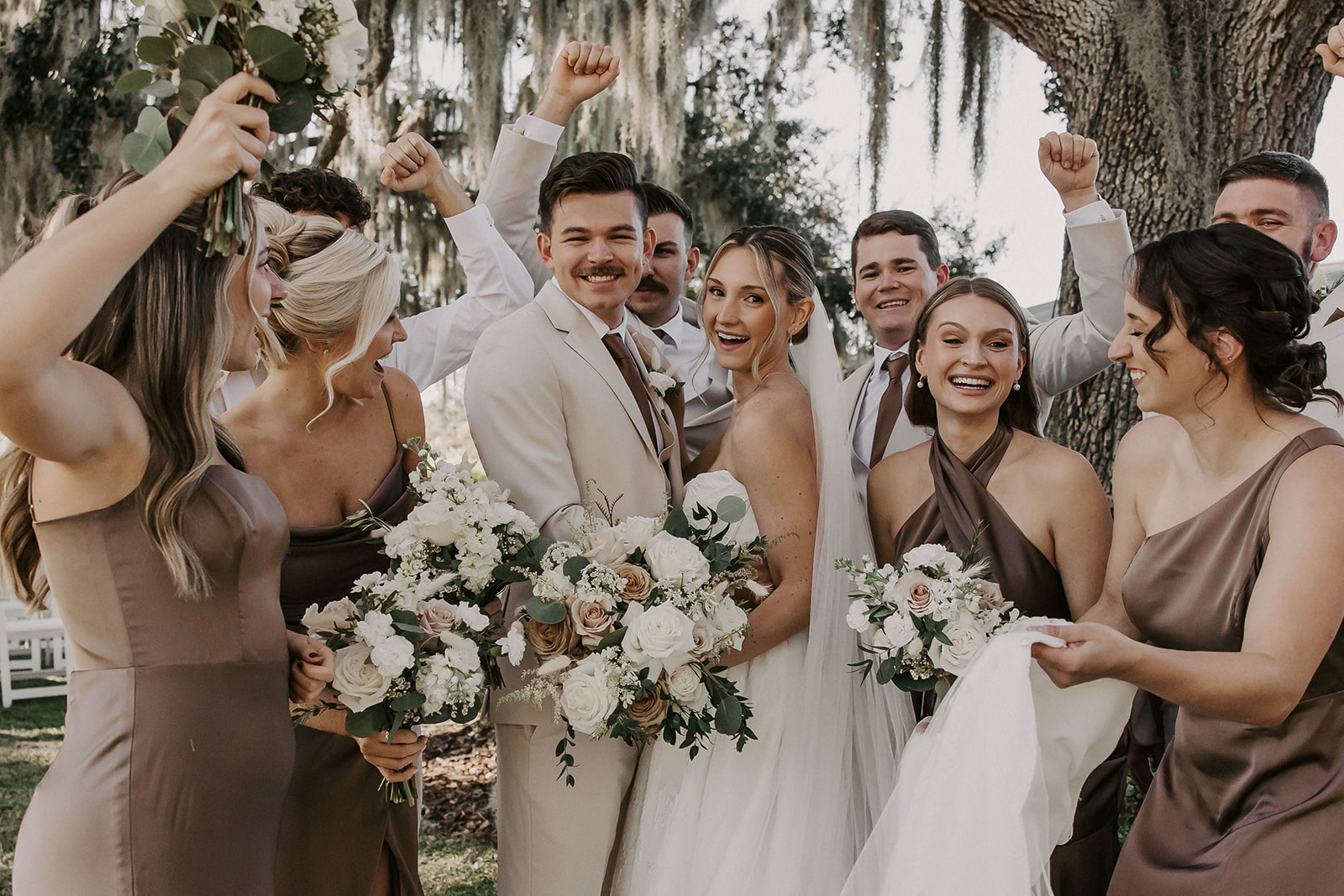 wedding party celebration la hacienda snow hill brooksville florida - A Fall Wedding at La Hacienda on Snow Hill in Brooksville, FL Joyful bride and groom surrounded by cheering bridesmaids in mauve satin dresses and groomsmen in tan suits holding white and blush rose bouquets at La Hacienda on Snow Hill wedding venue in Brooksville Florida near Tampa