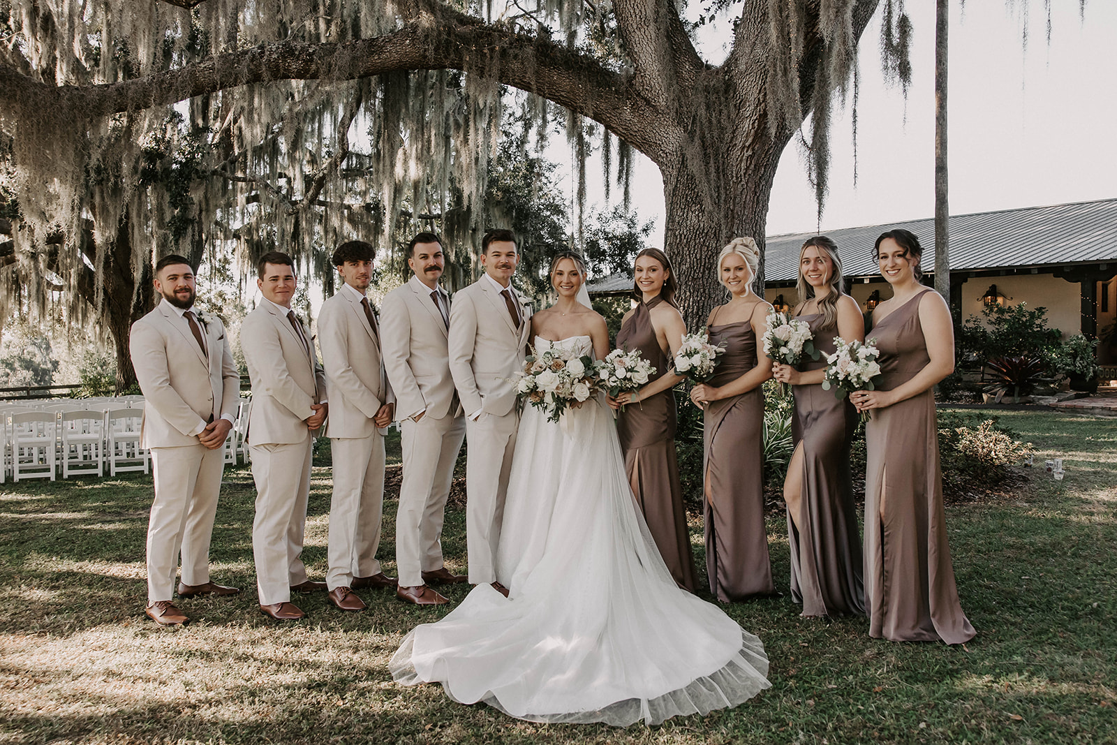 wedding party portrait la hacienda snow hill brooksville florida - A Fall Wedding at La Hacienda on Snow Hill in Brooksville, FL Bride and groom with bridesmaids in taupe satin gowns and groomsmen in cream suits posing under a Spanish moss-draped oak tree at La Hacienda on Snow Hill wedding venue in Brooksville Florida near Tampa